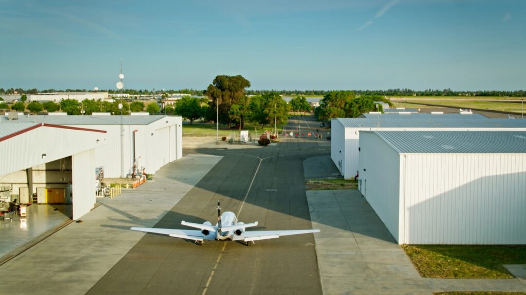 Wide Shot of Private Jet at Small Airfield Surrounded by Airplane Hangars